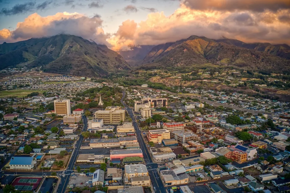 Aerial view of town of Wailuku in Maui, Hawaii with mountains in background against cloudy sunset sky.